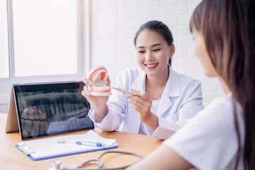 Happy smiling Asian female dentist doctor examining teeth model diagnosing patient dental hygiene using tablet x-ray technology, healthcare expert orthodontist specialist hospital meeting office room