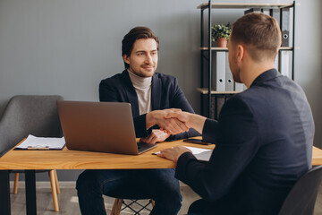 Two smiling successful young businessmen shaking hands at a business meeting in the office