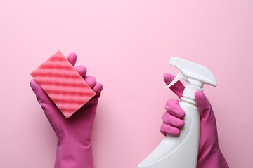 Woman in rubber gloves holding sponge and detergent on pink background, top view
