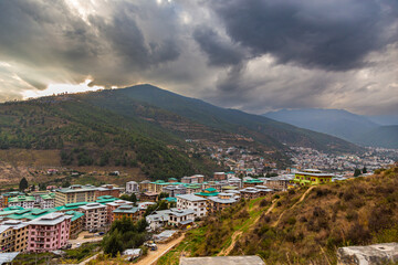 Thimphu, Bhutan - October 26, 2021: Aerial view cityscape of Bhutan capitol city. Top view with dramatic cloudy sky over the town. Largest city in Bhutan in a mountain valley. Houses with green roof