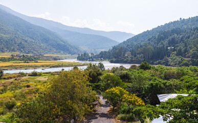 Wide angle panorama over the free wild open landscape of Bhutan. The mountain of the Himalayas in the haze on the horizon. A river meanders through the valley, veil clouds in the sky