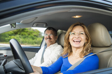 Closeup shot of a middle-aged Hispanic couple smiling in a car with the wife driving