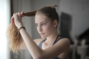 Closeup shot of a young blonde girl stretching her ponytail in her room
