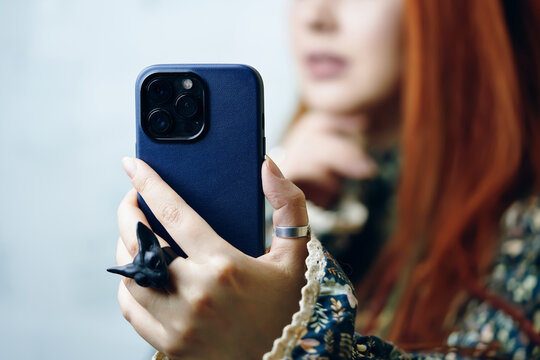 Female's hand with gothic ring holding smartphone in blue case. Woman blogger takes selfie on iPhone 13 pro. Focus on foreground. Gadget with triple-lens camera. Bishkek, Kyrgyzstan - January 24, 2022