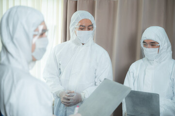 Group of medical professionals wearing ppe kit with eyeglass and gloves reading report and checking progress on female patient infected with coronavirus