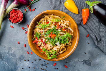 Udon noodles with vegetables on wooden bowl on grey table top view