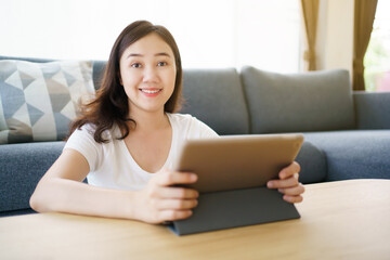 Happy Asian young woman relaxing in the living room and watching a contents and chatting with her friends and drawing an illustration on tablet. Woman enjoy watching video and drawing on tablet.