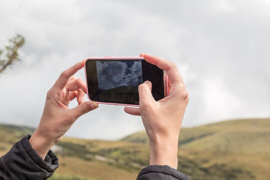 holding with both hands a cell phone to take a photo of a landscape with mountains in the day, technological device and screen detail