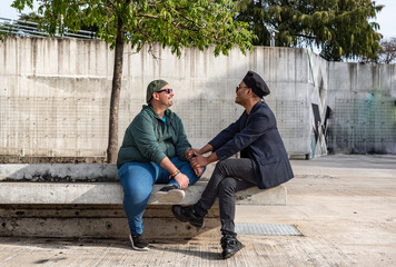 Gay male couple talking and holding hands while sitting on a bench outdoors