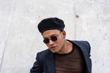 Young latin gay man with make-up on wearing a fashionable hat and sunglasses, isolated on a White background looking at camera. LGBT. 