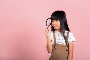 Asian little kid 10 years old funny looking through magnifying glass at studio shot isolated on...