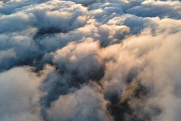 Aerial view from airplane window at high altitude of dense puffy cumulus clouds flying in evening