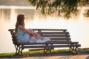 Lonely woman sitting on lake side bench enjoying warm summer evening. Solitude and relaxation...