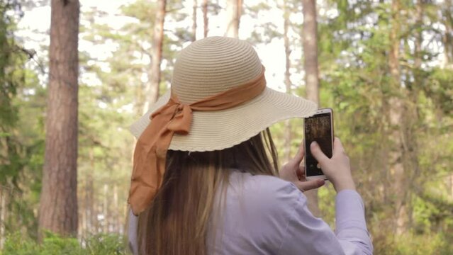 Attractive woman with hat taking photos and videos of beautiful forest