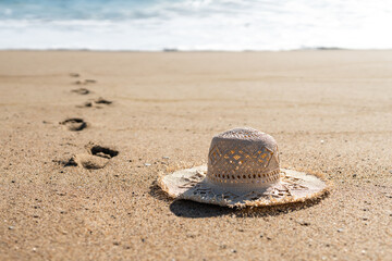 Woman's straw beach hat on sand on the beach, and foot prints leading to the sea. Beautiful sunny...