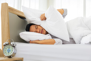 Man lazily cover his ear with pillow for the loud wake up noise from alarm clock in the morning...