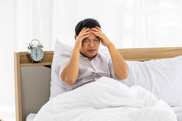 Unhappy man sitting in his bed with stress and worrisome which resulted in headache and migraine problem