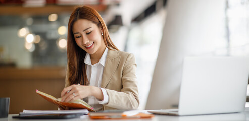 Fototapeta na wymiar Smiling Asian businesswoman working on a laptop in a modern office, Concept of accountant, financial, expert, analyze, business report graph finance chart corporate economy, banking market research 