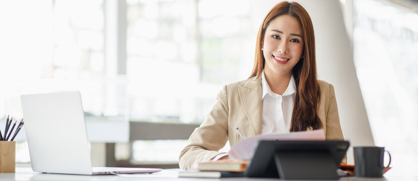 Smiling Asian businesswoman working on a laptop in a modern office, Concept of accountant, financial, expert, analyze, business report graph finance chart corporate economy, banking market research 