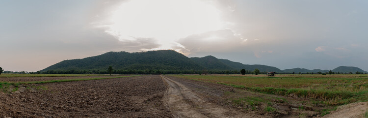 Dirt road in a countryside with hight mountain and the sun light from the sky, countryside view in the evening sunset.