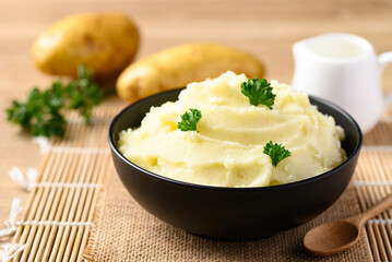 Mashed potato with parsley in black bowl on wooden table