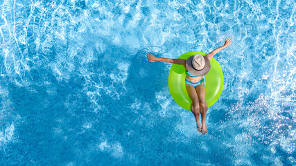 Active young girl in swimming pool aerial drone view from above, teenager relaxes and swims on inflatable ring donut and has fun in water on family vacation, tropical holiday resort