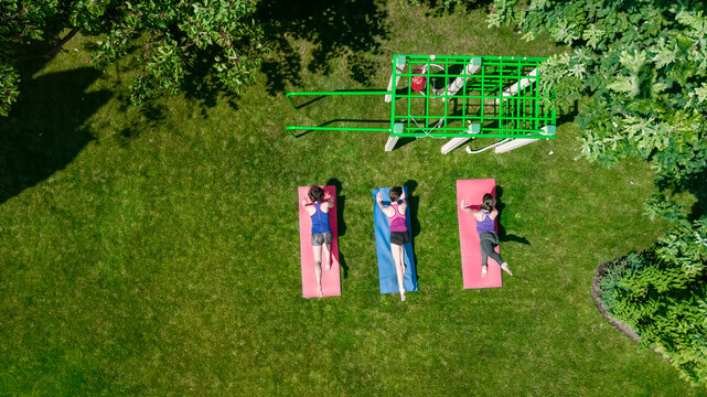 Fitness and sport outdoors, group of active girls doing workout in park, healthy women exercising on green grass, aerial drone view from above