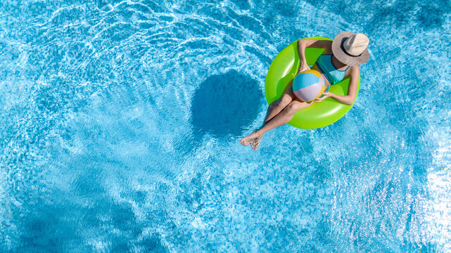 Active young girl in swimming pool aerial drone view from above, teenager relaxes and swims on inflatable ring donut and has fun in water on family vacation, tropical holiday resort