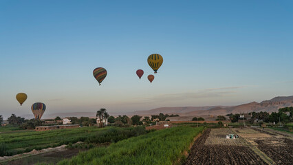 Bright balloons are flying in the blue sky. Below - cultivated green fields. The sand dunes of the...