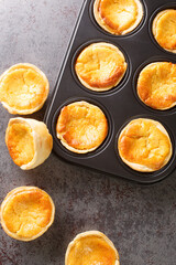 Tarts Queijadas with custard close-up in a baking dish on the table. vertical top view from above