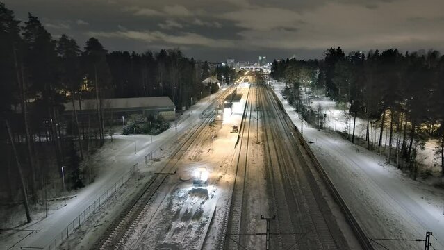 Vantaa.Finland-December 29.2021: Small tractors pushing snow off of the train station platform in Vantaa. Maintaining transportation during the nordic winter. Aerial shot. Drone slowly moving forward.