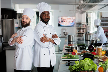 Multiethnic male cooks standing in restaurant professional kitchen with arms crossed while...