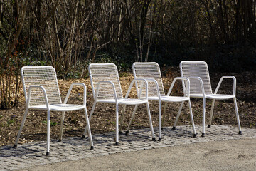 Row of four white metal grid chairs outdoors in the ornamental garden