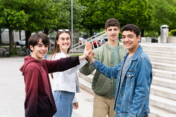 Group of positive teenagers giving high five outdoors