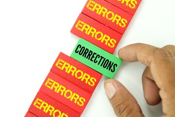 hand holding a wooden board with the words corrections and errors on red boards