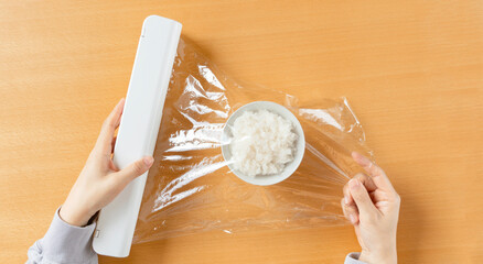 A woman who preserving the rice with cling wrap for foods. 食品用のラップを用いてご飯を保存する女性。 - obrazy, fototapety, plakaty