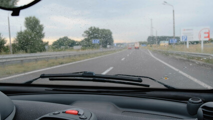 Fototapeta na wymiar Car windshield during light rain. Car moves by rainy day along the highway, the wind blows off raindrops from front glass of car