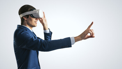 Young man working in virtual reality office in VR glasses, presses his finger virtual interface on abstract light grey backdrop. Innovate and future technology concept, close up