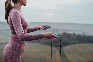Side View of Unrecognisable Young Woman Holding Skipping Rope, Girl Working Out Outdoors on the Hill - obrazy, fototapety, plakaty