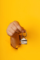 Male hand with metal house and key through a hole in yellow paper wall. House sale and rent concept. Vertical image