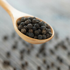 Whole black peppercorn in a wooden spoon on wooden background.