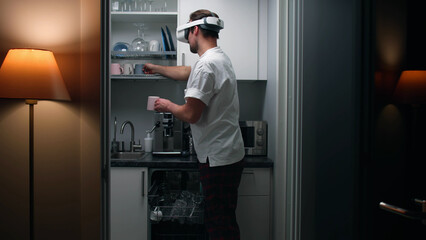 Young man in virtual reality goggles unload dishwashing machine in small kitchen