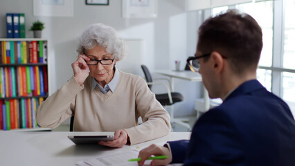Senior woman meeting financial advisor and looking at charts on digital tablet - obrazy, fototapety, plakaty