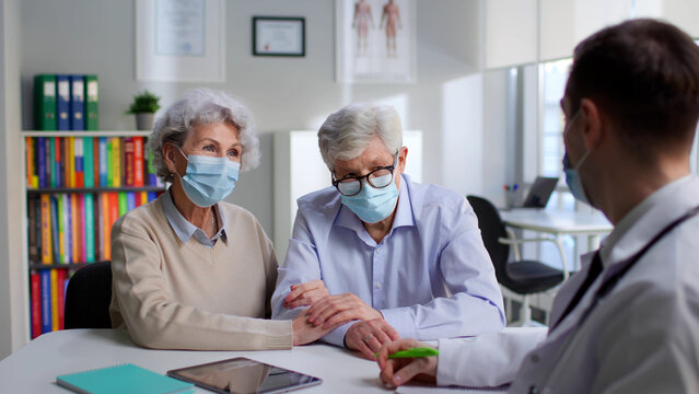 Senior Couple In Safety Mask Having Appointment With Doctor In Modern Medical Center