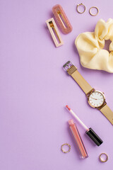 Makeup beauty concept. Top view vertical photo of scrunchy lip gloss gold wrist watch rings and barrettes on isolated pastel violet background