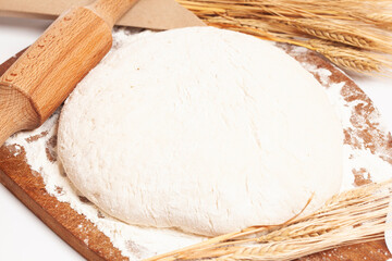 Fresh yeast dough with wheat ears on cutting board with rolling pin