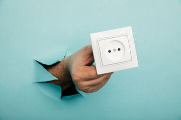 Male hand holds socket in torn hole of blue background