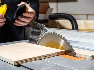 Close up of table saw cutt of  birch plywood sheet   and carpenter with ear defenders selective...