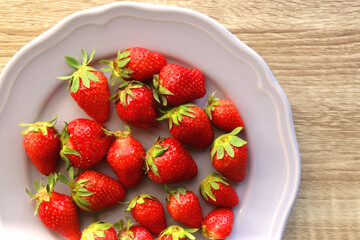 Lilac plate full of fresh strawberries on wooden table. Flat lay.