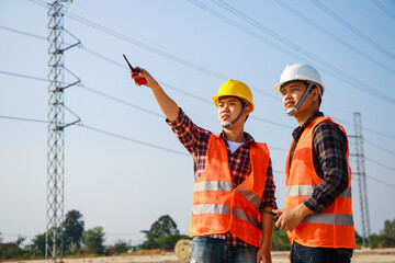 Two Electrical engineers with a high voltage electricity pylon at sunset background.